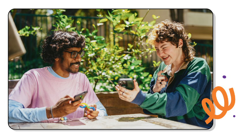 Two friends laugh together as they share a phone screen