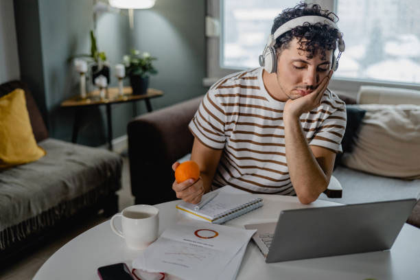 A man wearing a stripy t-shirt and headphones watches his tablet screen while snacking